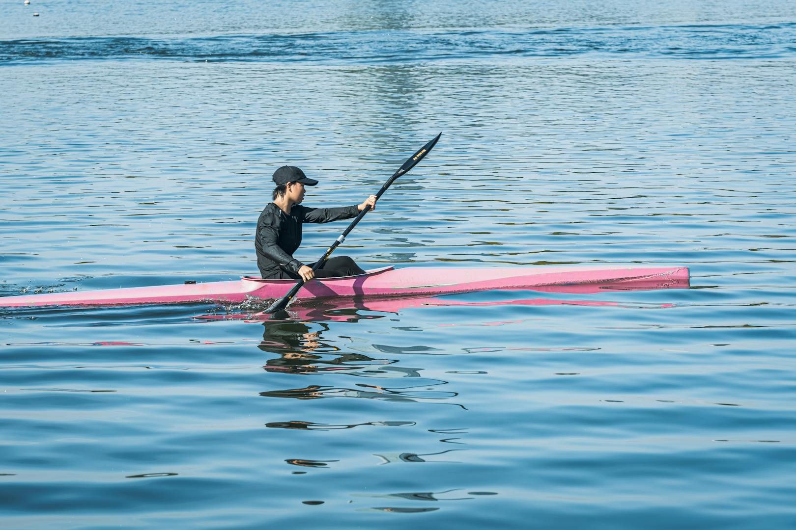 A person kayaking on calm waters in a vibrant pink kayak under clear skies.